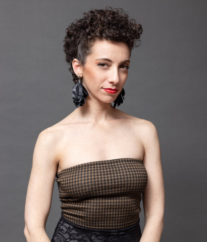 Headshot of Latin Female wearing crop top and long dangly earrings, with curly hair pulled up.