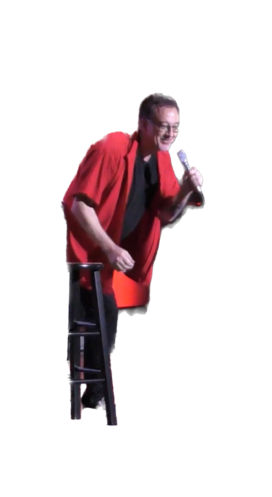 Man in red shirt holding a microphone leaning over a stool.