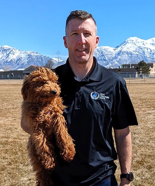 Portrait of a caucasian man holding a poodle mix dog in front of a beautiful mountain scene